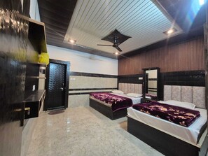 Habitación de hotel con dos camas, un ventilador de techo, un espejo grande y un armario de madera oscura.