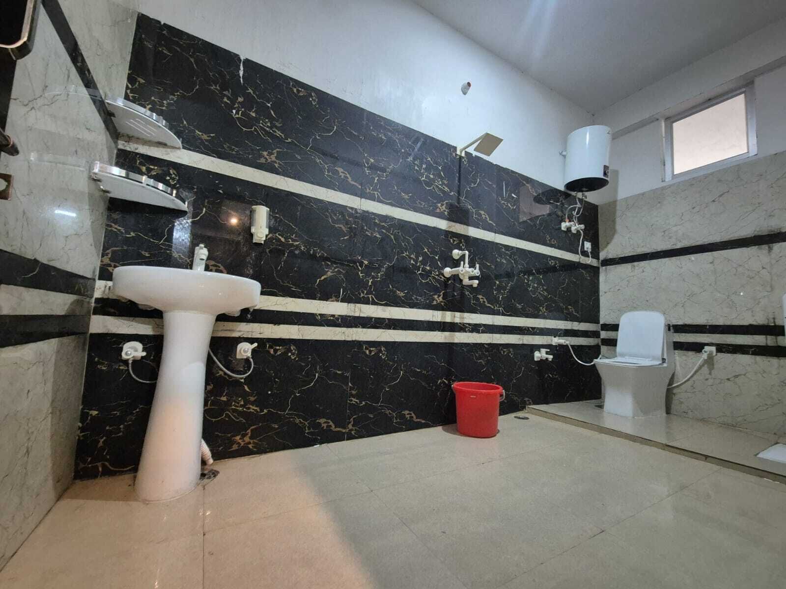 Un baño con un lavamanos blanco, un inodoro y una ducha. Las paredes tienen un diseño de mármol negro con detalles blancos.