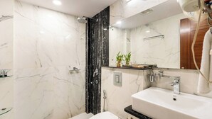 A modern bathroom with a white marble shower, a white toilet, a white sink with a black countertop, and a mirror above the sink. - TIM Sector 51, ARTEMIS HOSPITAL 1 min walk, FORTIS & MEDANTA 4 mins drive (Gurugram)