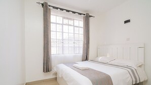 Een slaapkamer met een bed, gordijnen, een raam en een lichtschakelaar aan de muur.