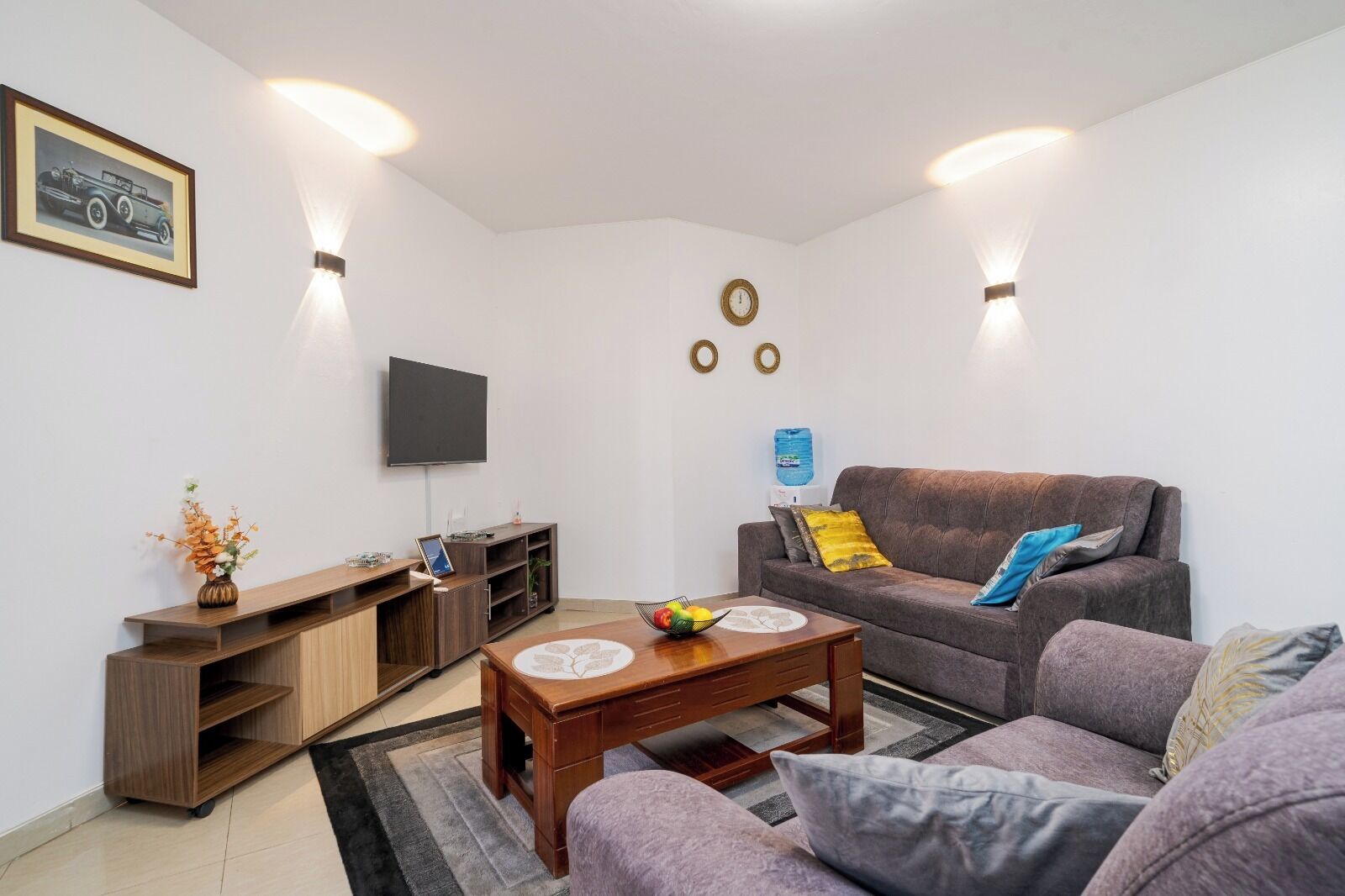 A living room with a sofa, coffee table, TV, and a wall-mounted shelf.