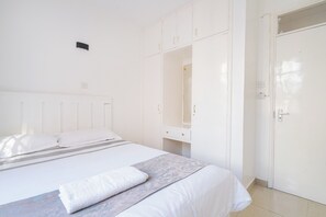 Une chambre à coucher blanche avec un lit, une table de chevet, une armoire et une porte.