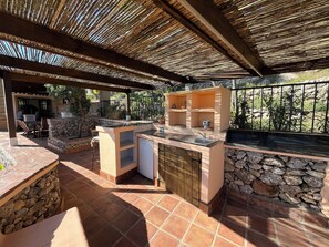 Enjoy cooking under the shade of a covered outdoor kitchen with a sink and stone countertop.