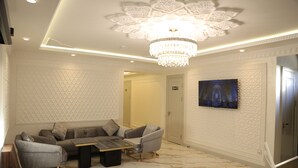 Un soggiorno moderno con un lampadario, una coppia di divani e una televisione a schermo piatto fissata al muro.