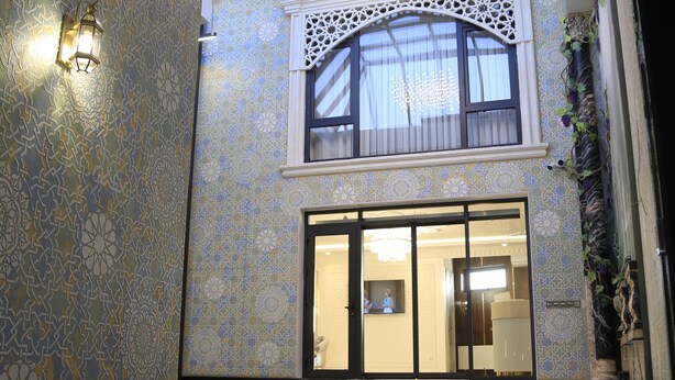 Un ampio atrio con soffitto alto, pareti decorate e vista su una stanza al secondo piano attraverso una porta in vetro.