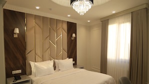 A modern hotel room with a large bed, a nightstand, a chair, and a chandelier. - Tillokori Plaza (Samarkand)