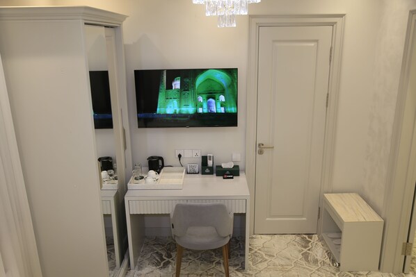 A small room with a desk, chair, and a television displaying a building. - Tillokori Plaza (Samarkand)