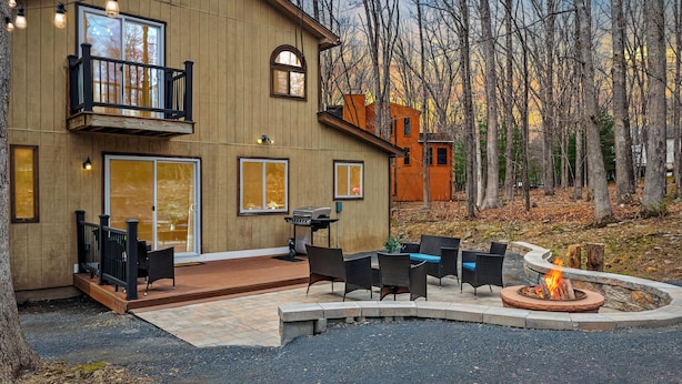 A two-story house with a balcony, a patio with outdoor furniture, and a fire pit. - Lake Access + Pools + Sports Complex | Near Skiing & Hiking | Foxden (East Stroudsburg)
