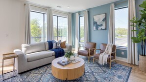 A modern living room with a sofa, two armchairs, a coffee table, and a large window with curtains. - Stylish Condo • Private Balcony • Near Germantown + Broadway | The Heights (Nashville)