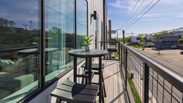 A balcony with a table and chairs, a potted plant, and a view of the street and buildings. - Stylish Condo • Private Balcony • Near Germantown + Broadway | The Heights (Nashville)