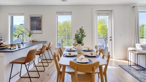 A modern kitchen with a dining area, large windows, and a view of the outdoors. - Stylish Condo • Private Balcony • Near Germantown + Broadway | The Heights (Nashville)