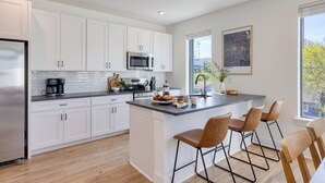 A modern kitchen with white cabinets, stainless steel appliances, and a central island with bar stools. - Stylish Condo • Private Balcony • Near Germantown + Broadway | The Heights (Nashville)