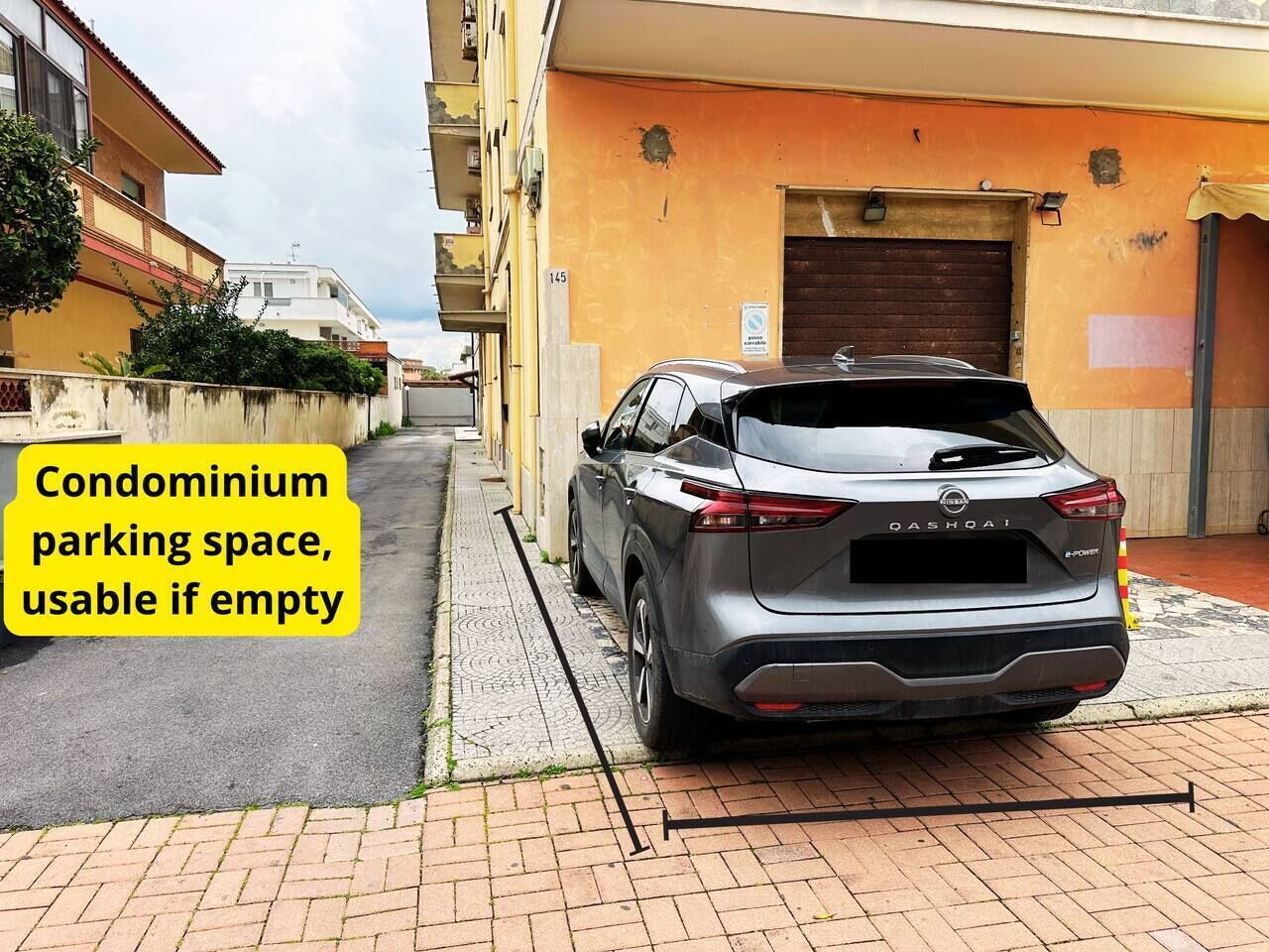Une voiture garée dans une rue étroite, avec un immeuble jaune sur le côté droit.