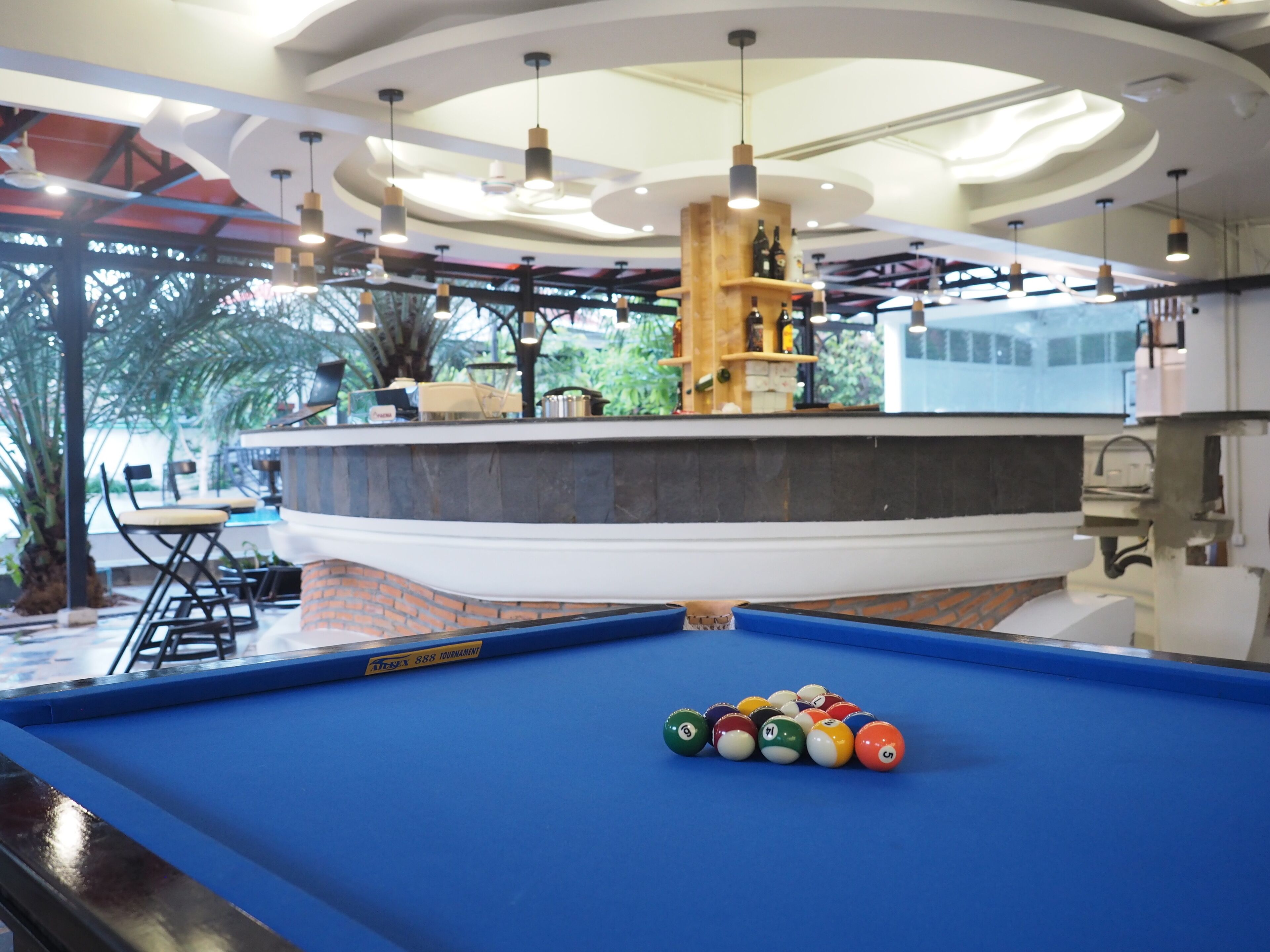 Une table de billard avec des billes, un bar avec des étagères remplies de bouteilles, et un espace détente avec des chaises et des tables.