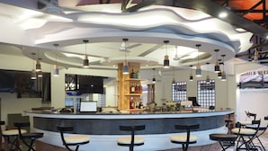 Uma área de bar moderna com balcão curvo, vários bancos e iluminação suspensa.