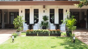 Pátio com área de estar, plantas em vasos e fachada de edifício com janelas e portas.