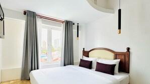Quarto de hotel moderno com uma cama grande, piso de madeira e vista para edifícios lá fora.