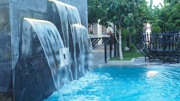 Piscina com cascata, cercada por muros de pedra e vegetação.
