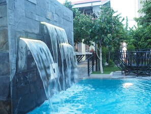A swimming pool with a waterfall feature, surrounded by stone walls and greenery. - Activate C3 Hostel (Phnom Penh)