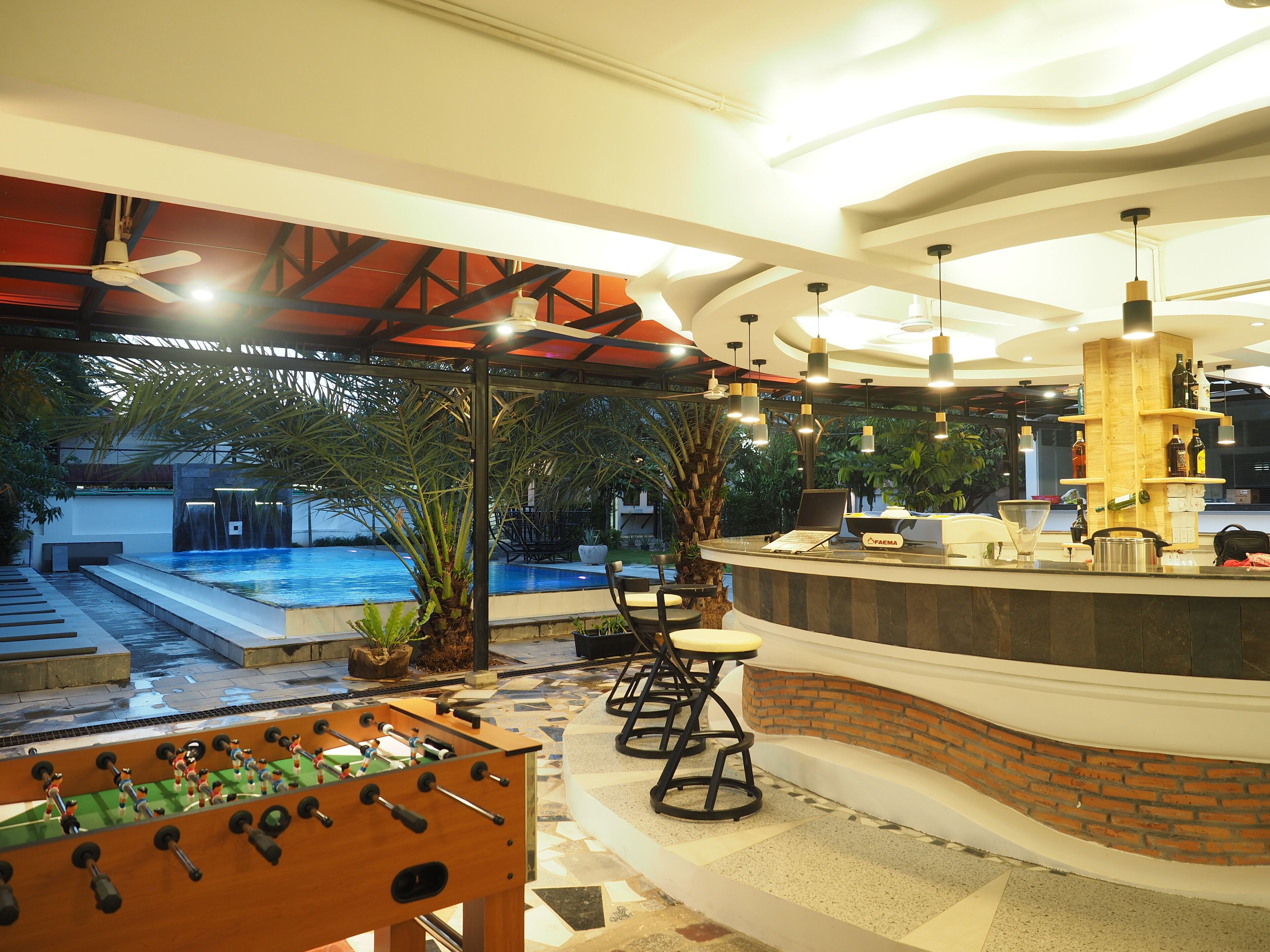 A pool area with a foosball table, a bar with a wooden counter, and a seating area with chairs and stools.