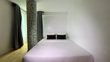 Un dormitorio minimalista con una cama individual, piso de madera y un pilar de azulejos.