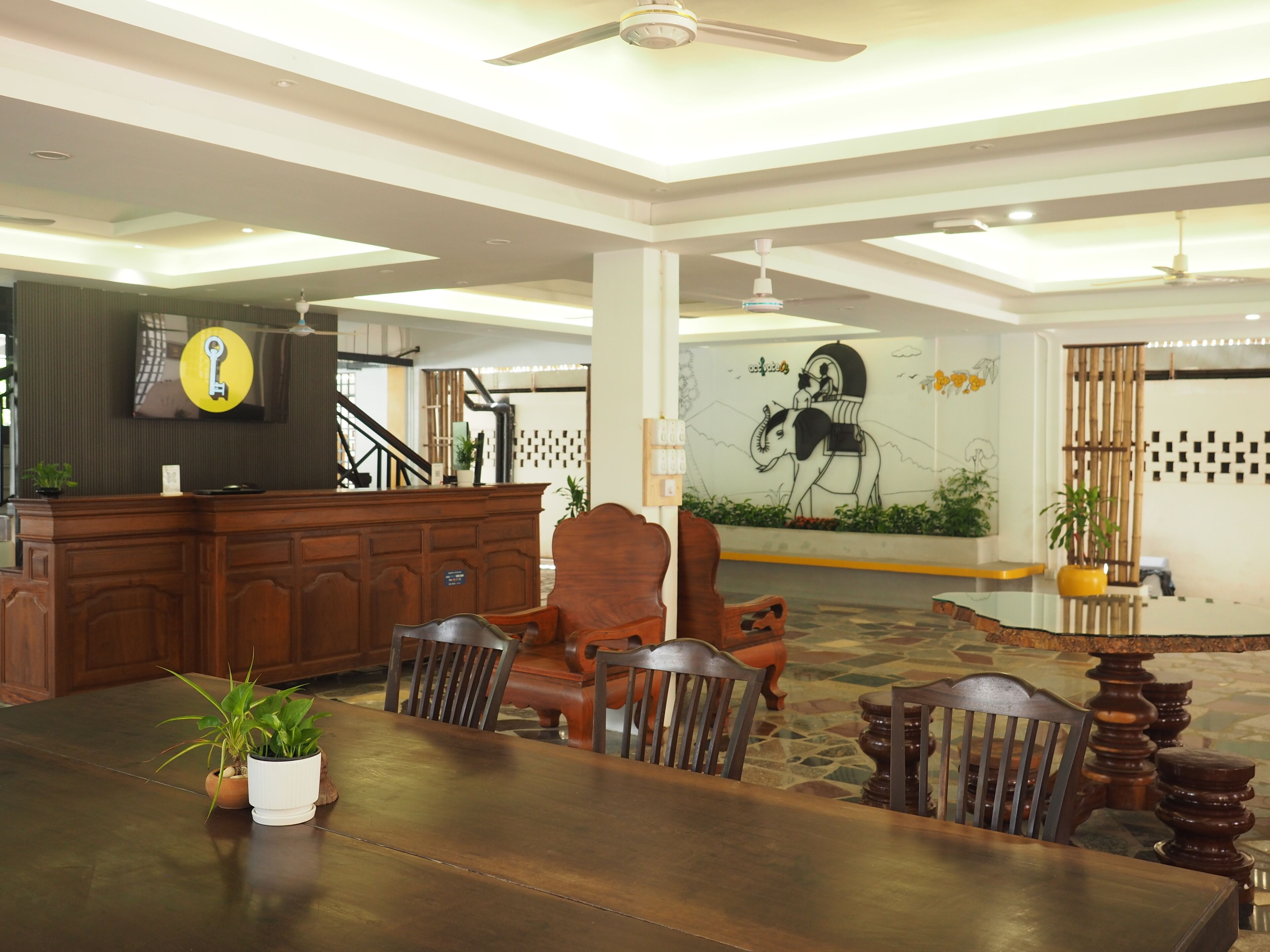 A spacious lobby with a reception desk, a large mural, and a dining area with wooden furniture.