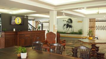 A spacious lobby with a reception desk, a large mural, and a dining area with wooden furniture.