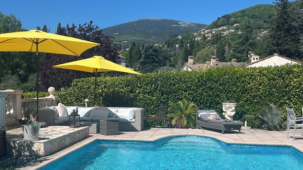 A swimming pool with a view of a hillside, surrounded by greenery and outdoor furniture.