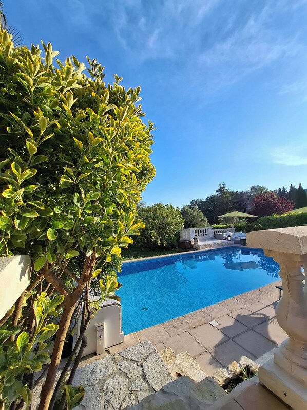 A swimming pool with a stone border, surrounded by greenery and a clear blue sky. - Villa Bibaou: 1 bedroom 2P ; a haven of peace between sea, mountains (Vence)