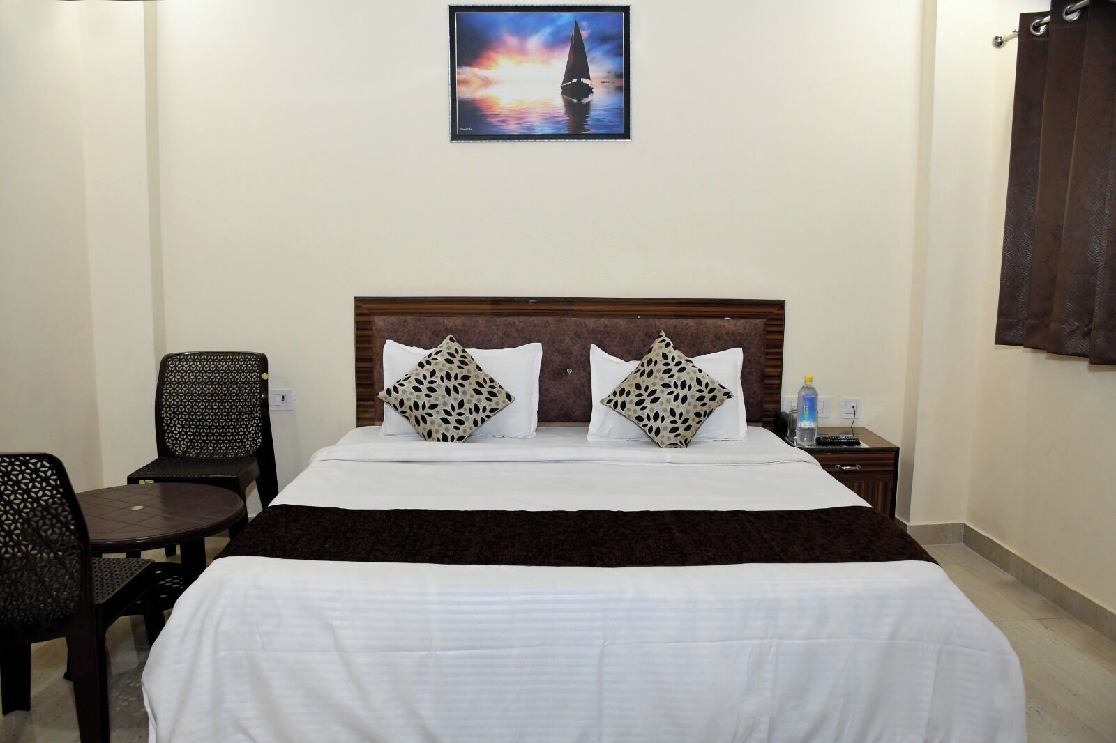 A hotel room with a bed, two pillows, a nightstand, a chair, and a painting on the wall.