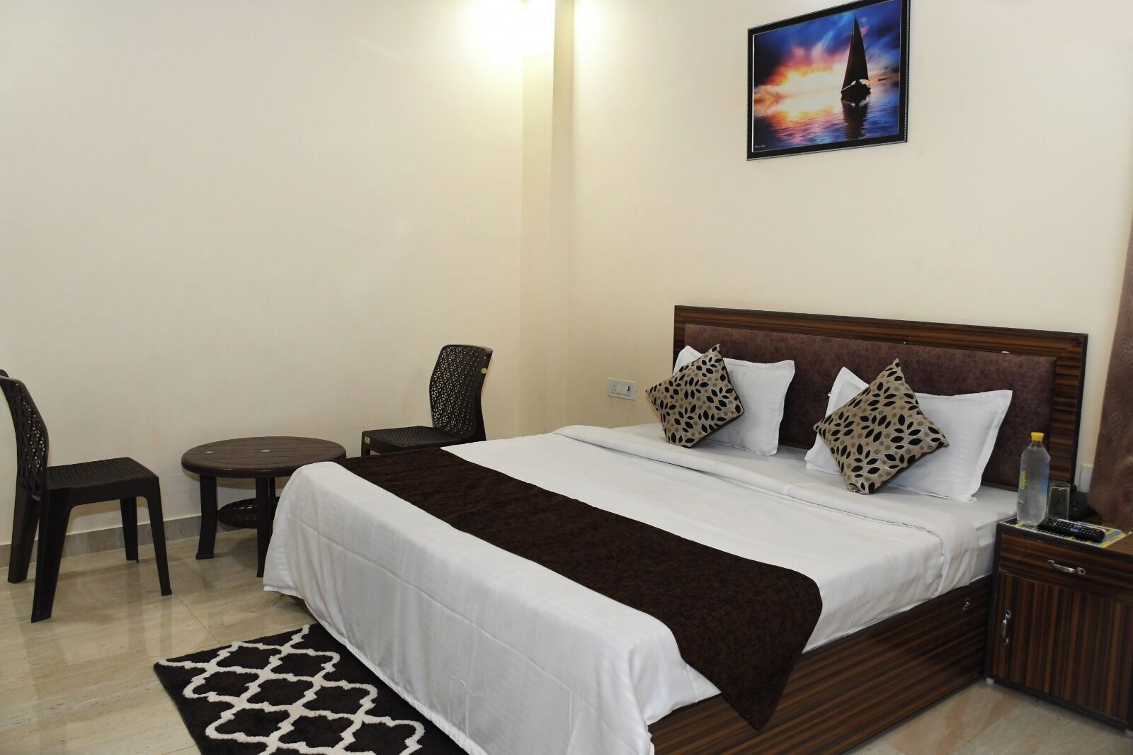 Une chambre d’hôtel bien rangée, avec un lit, deux chaises, une petite table et un tableau accroché au mur.