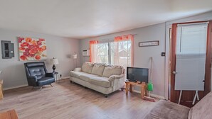 Un salon avec un canapé beige, un fauteuil noir, un téléviseur posé sur un meuble en bois et un tableau accroché au mur.