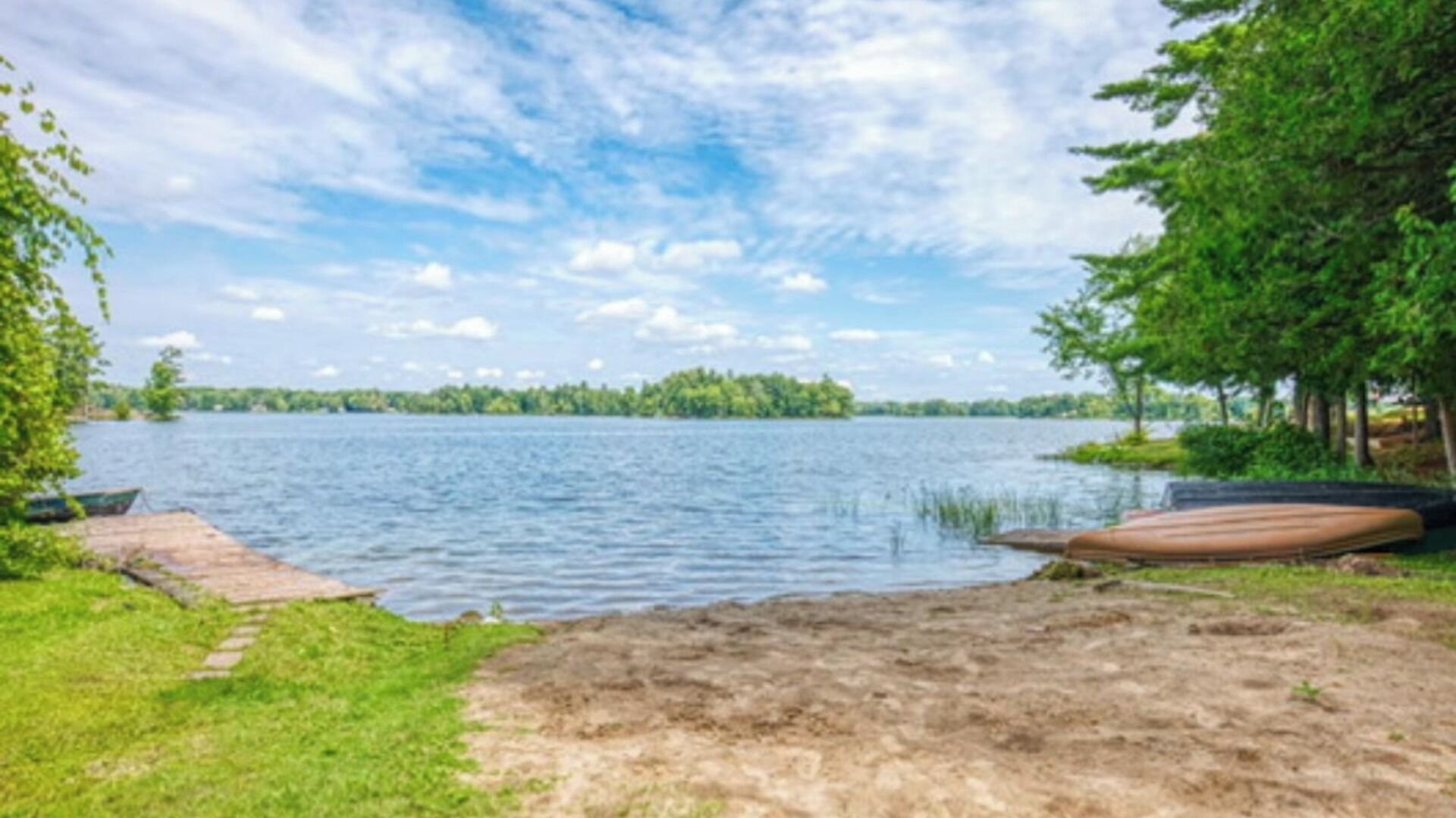 Vista de un lago con un muelle de madera, césped y árboles.