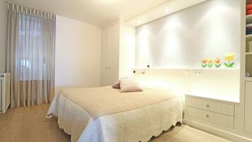 A bedroom with a bed, a bedside table, a wardrobe, and a window with curtains.
