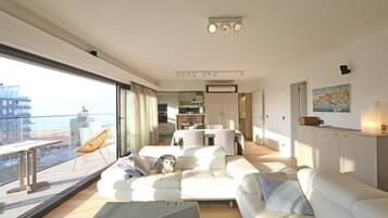 Een moderne woonkamer met een groot raam, een bank, een eethoek en uitzicht op de stad.