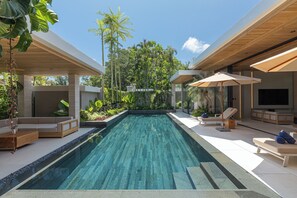 Un espace piscine extérieur moderne doté d’une piscine rectangulaire, de chaises longues et d’un écran de télévision.