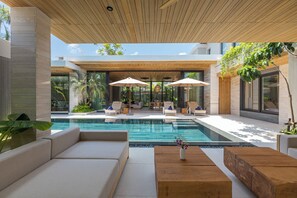 A modern pool area with lounge chairs, a wooden table, and a view of the pool. - Layana Residence (Choeng Thale)