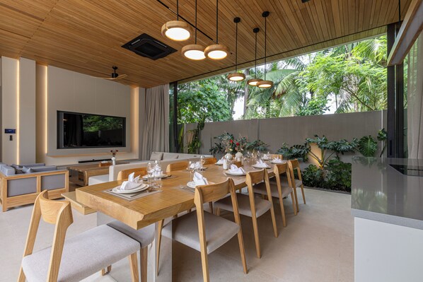 A modern dining area with a long wooden table set for a meal, surrounded by chairs. - Layana Residence (Choeng Thale)