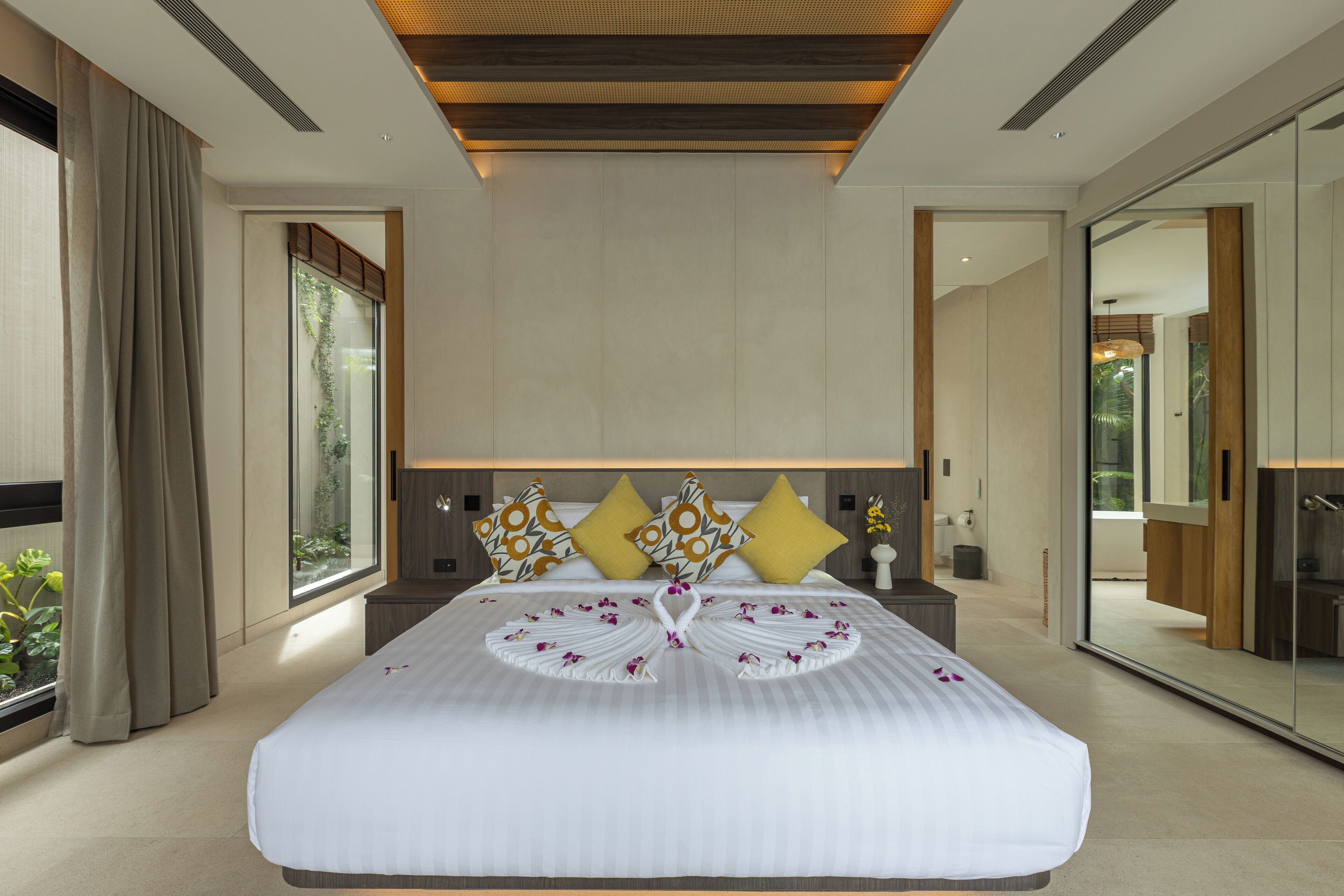 A modern hotel room with a large bed, a mirror, and a view of the outdoors.