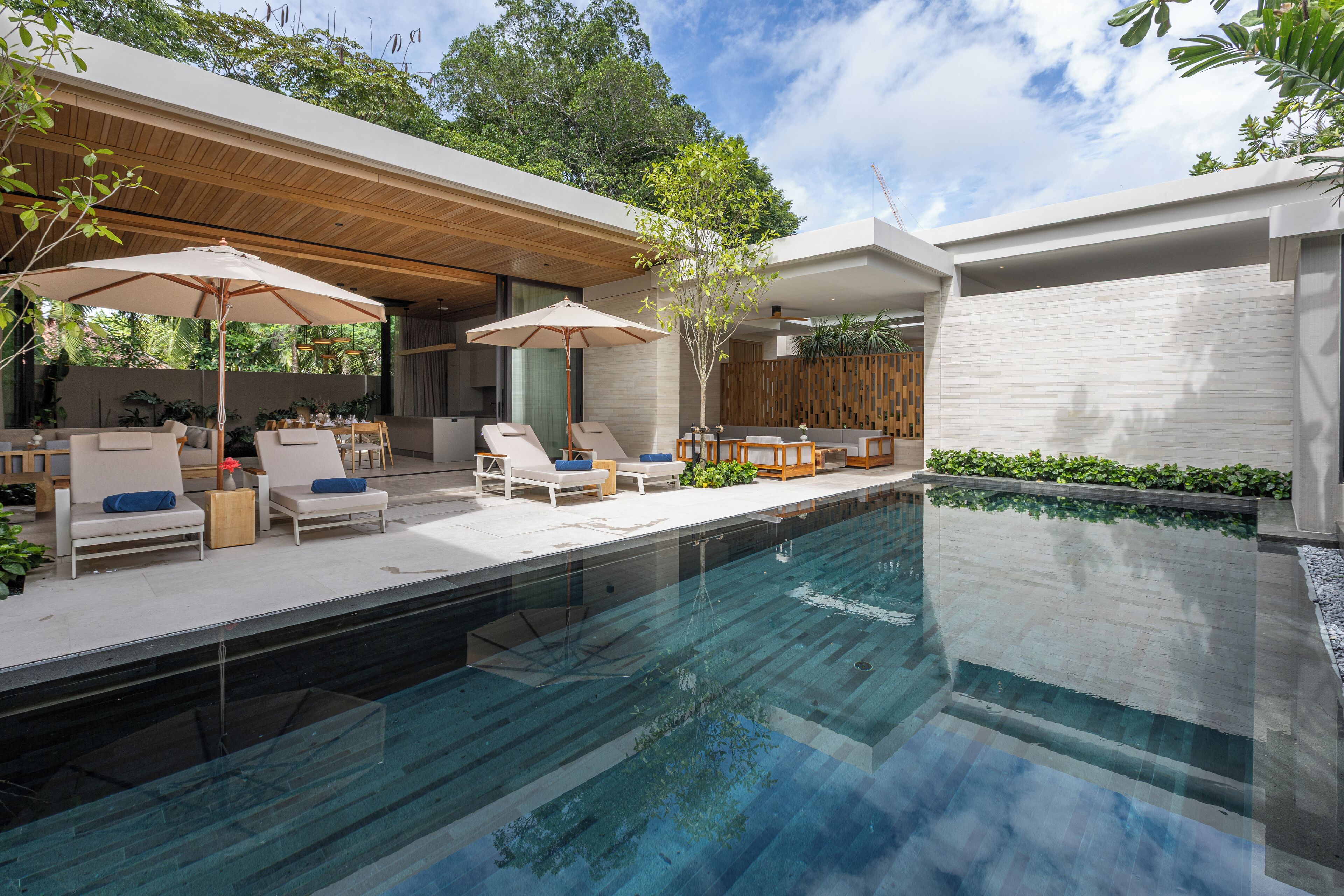A modern outdoor pool area with lounge chairs and umbrellas, surrounded by wooden decking and greenery.
