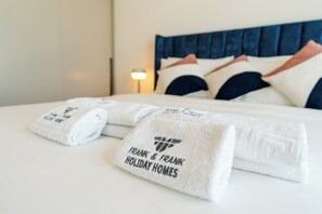 A neatly made bed with white linens and towels, a blue headboard, and a nightstand with a lamp. - Burj Khalifa & Fountain View | Living & Bedroom (Dubai)
