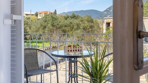 A balcony with a table and chairs, a potted plant, and a view of buildings and mountains.