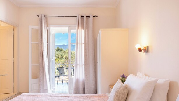 A bedroom with a bed, a nightstand, a wall-mounted lamp, and a view of a balcony with a chair and table.