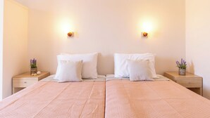 A double bed with a pink quilt, two white pillows, and two bedside tables with small potted plants.