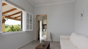 Amplia sala de estar con un sofá blanco, una mesa de centro de madera y vista a una cocina a través de un vano abierto.