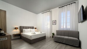 Une chambre moderne avec un lit, des tables de chevet, un canapé, une télévision et une fenêtre avec des rideaux.