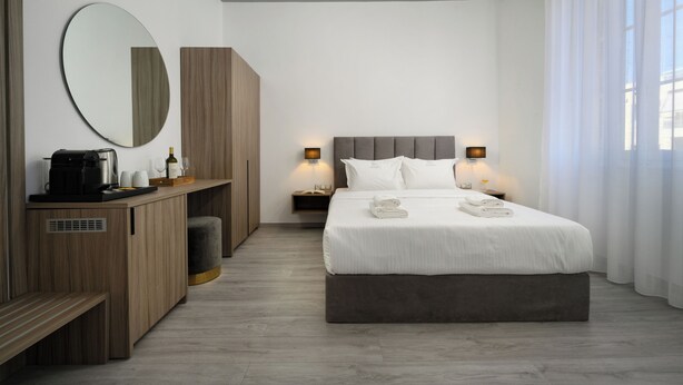 Une chambre d’hôtel moderne avec un grand lit, une table de chevet avec une lampe, un miroir et un banc en bois.