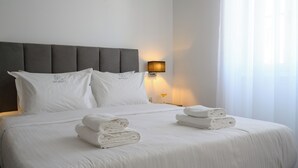 Un lit bien fait, avec du linge de lit blanc et des oreillers, une lampe de chevet et deux serviettes pliées posées sur le lit.