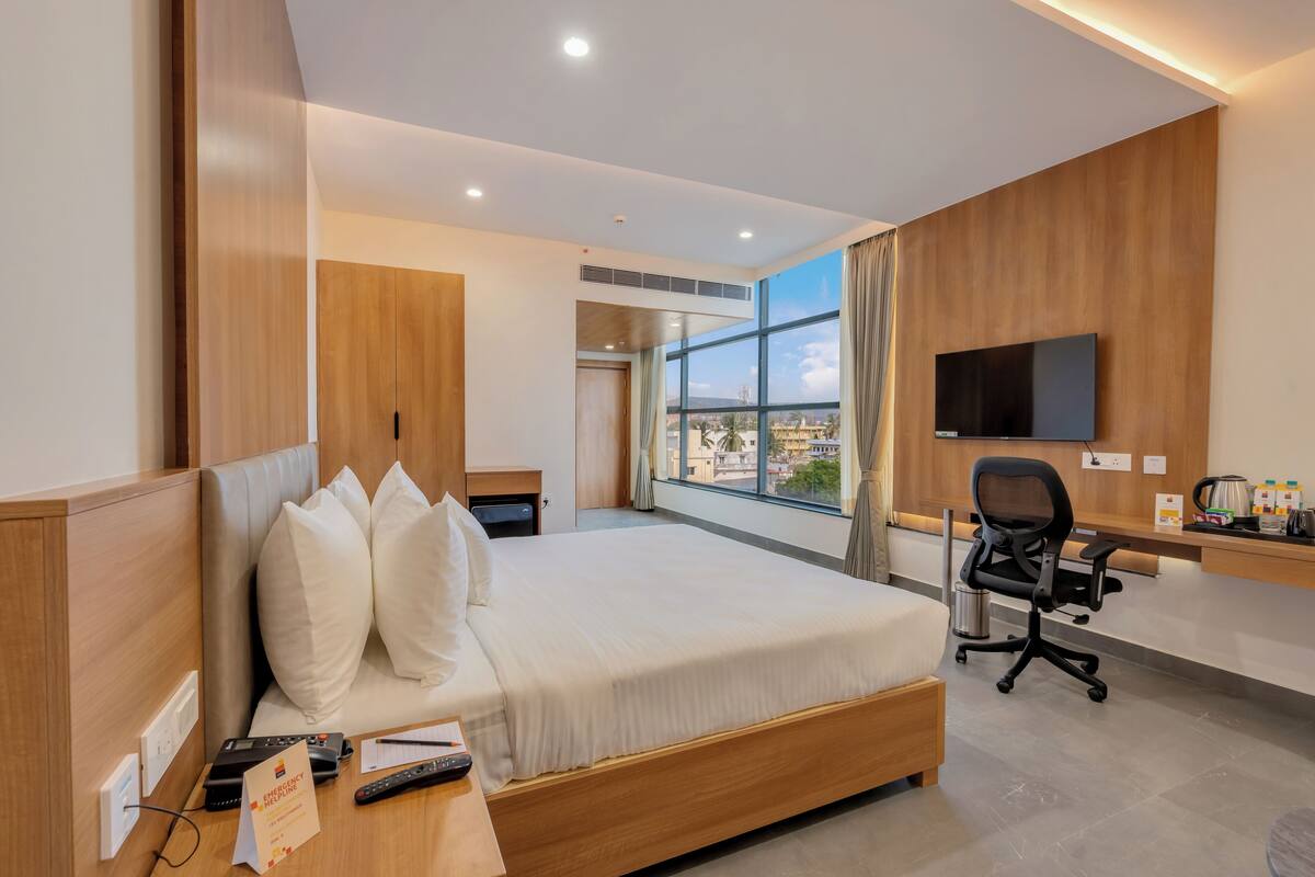 Habitación de hotel moderna con una cama grande, un escritorio con una silla, un televisor montado en la pared y una ventana con vistas a la ciudad.