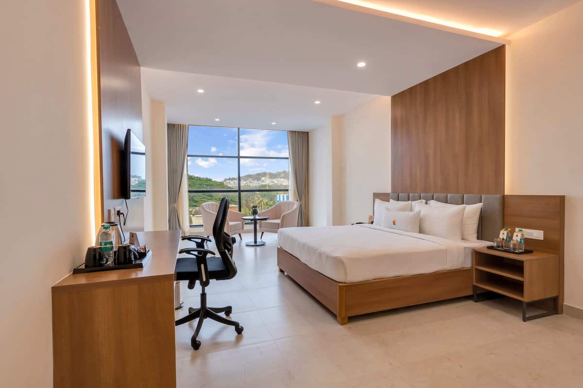 Habitación de hotel moderna con una cama grande, un escritorio con silla de oficina, televisor y vistas a la ciudad.